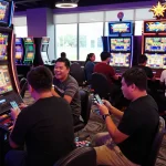 Sebuah adegan permainan yang hidup di kasino yang menampilkan pemain di sekitar mesin slot 'link gacor', suasana meriah yang dipenuhi kegembiraan dan lampu neon.